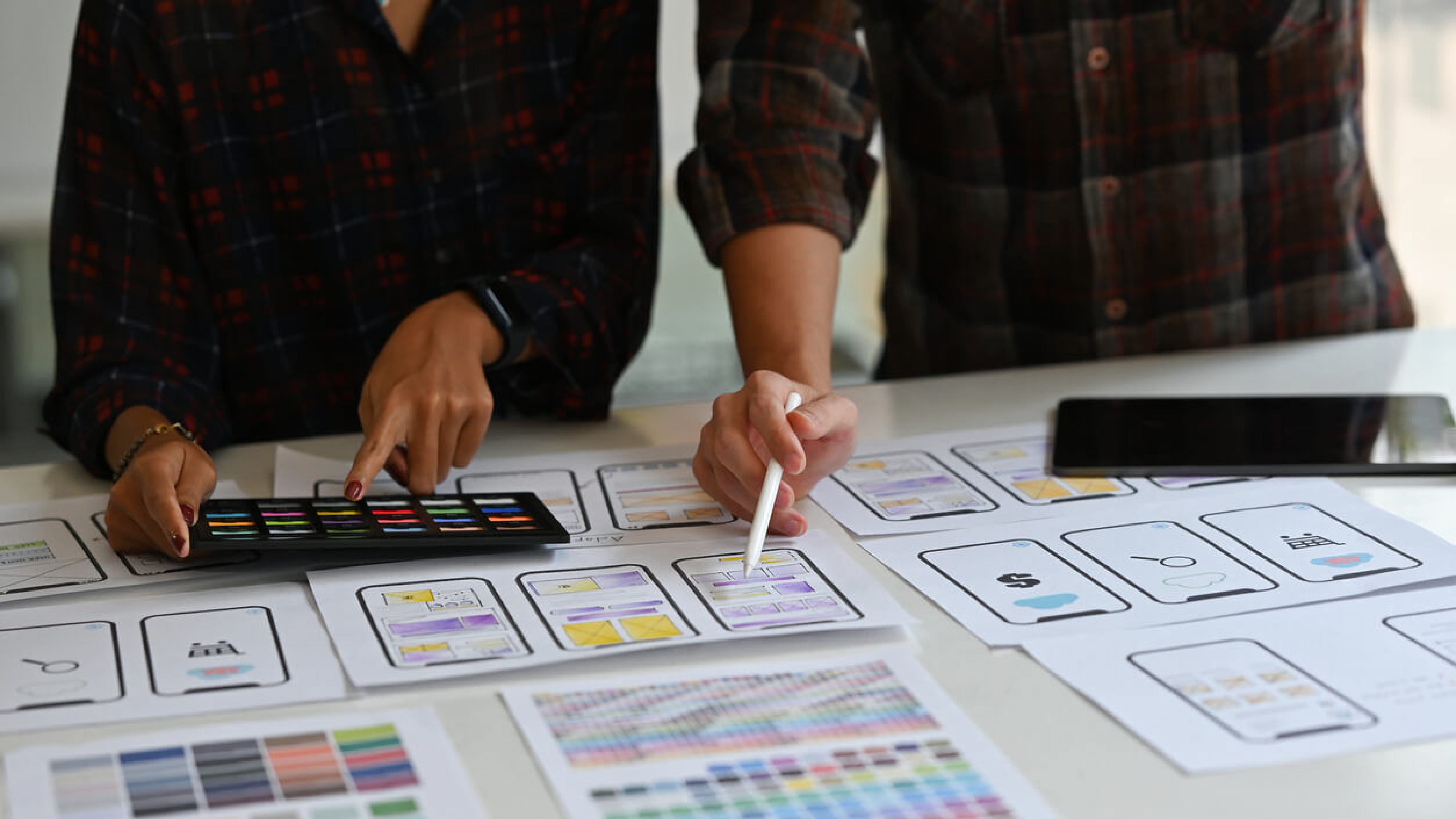 Two team members pointing to colors on sketches, deciding color palettes for an app or website.