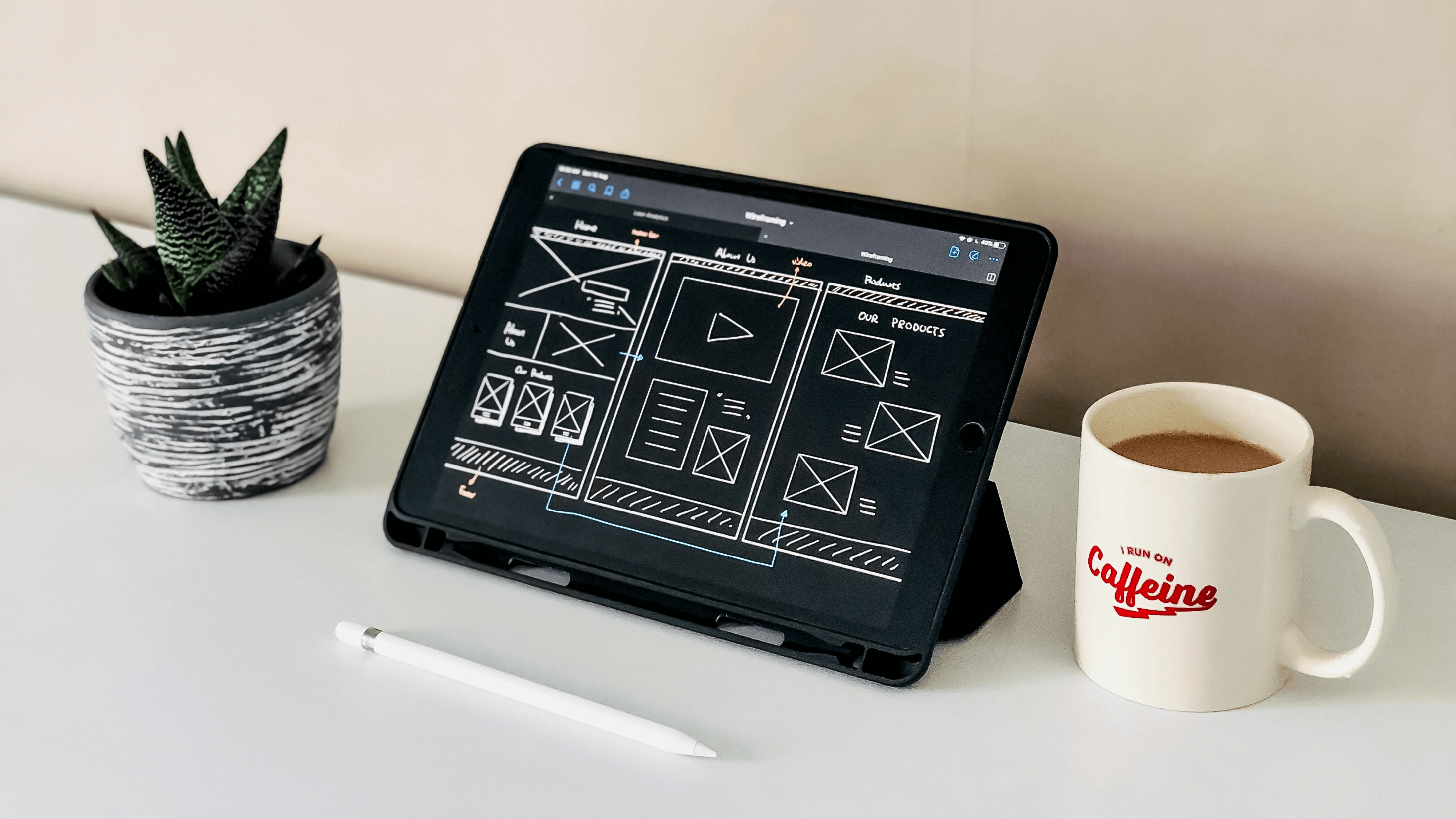 Coffee cup and iPad on desk displaying application wireframe.