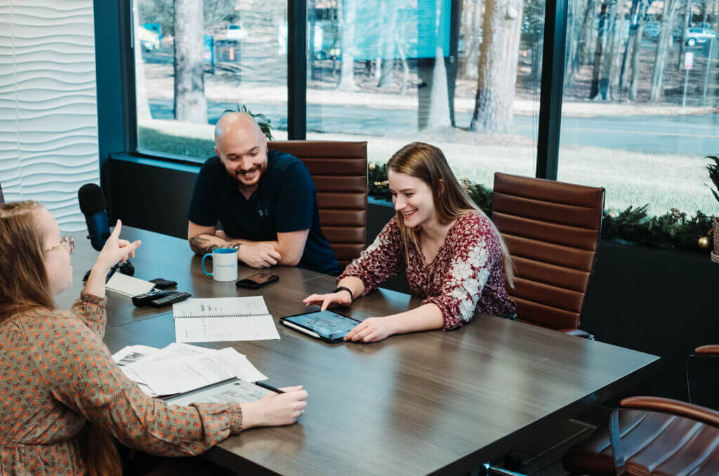 team smiling around a conference table, looking over notes, and an ipad